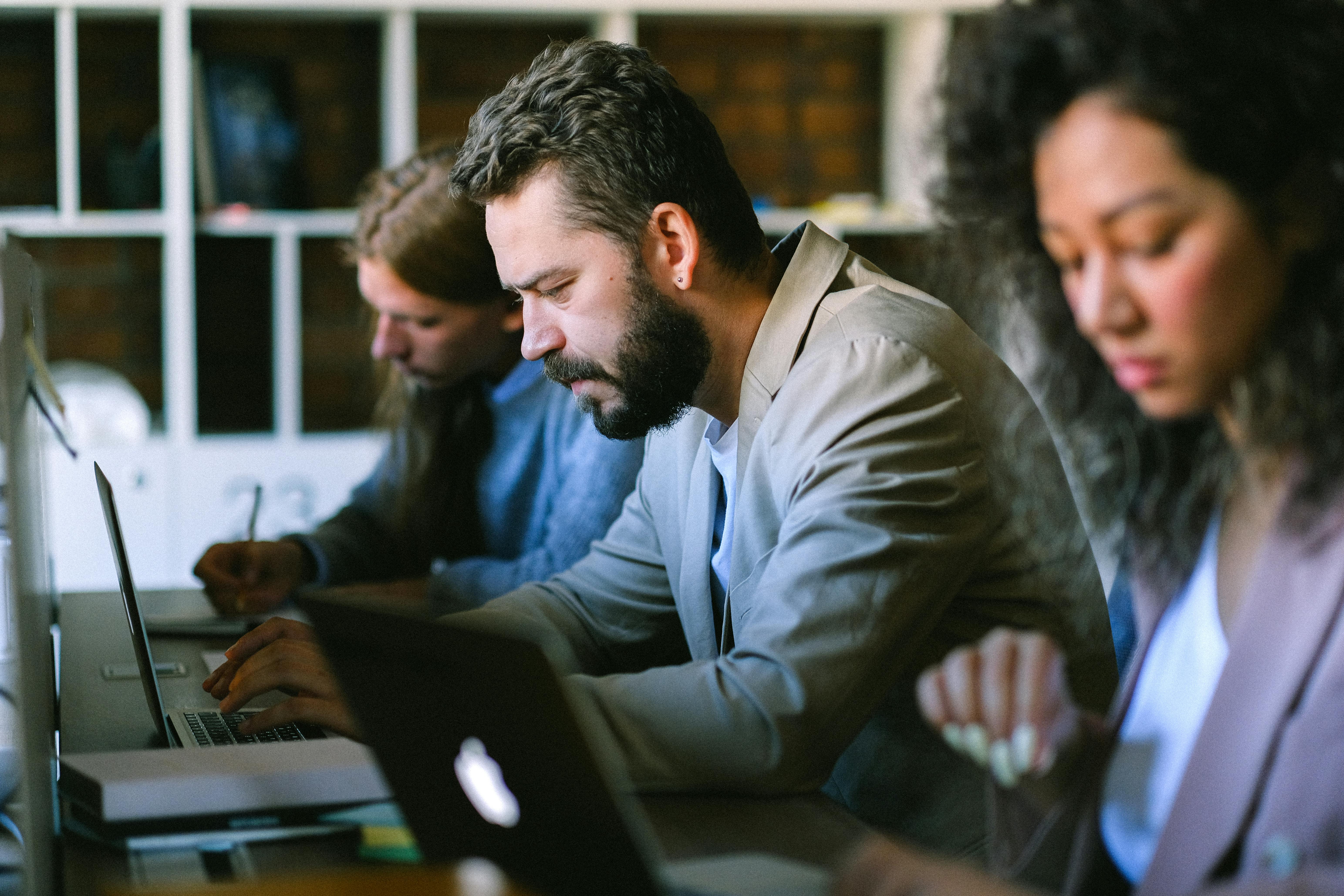 Workplace setting, three people working on computers (2 men, 1 woman)